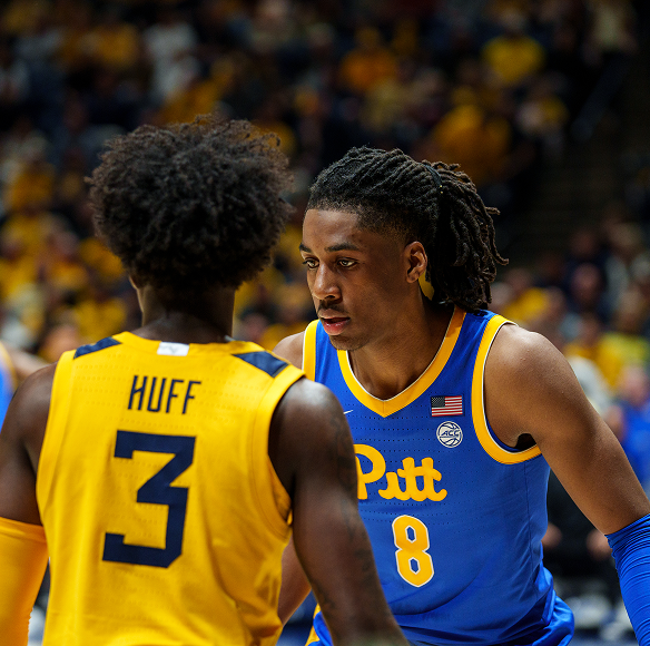 A close-up action photograph on a basketball court showing a University of Pittsburgh player wearing a blue and yellow jersey (#8) facing an opposing player seen from behind, who is wearing a yellow jersey with HUFF and the number 3 on the back. A crowded arena stands in the blurred background.