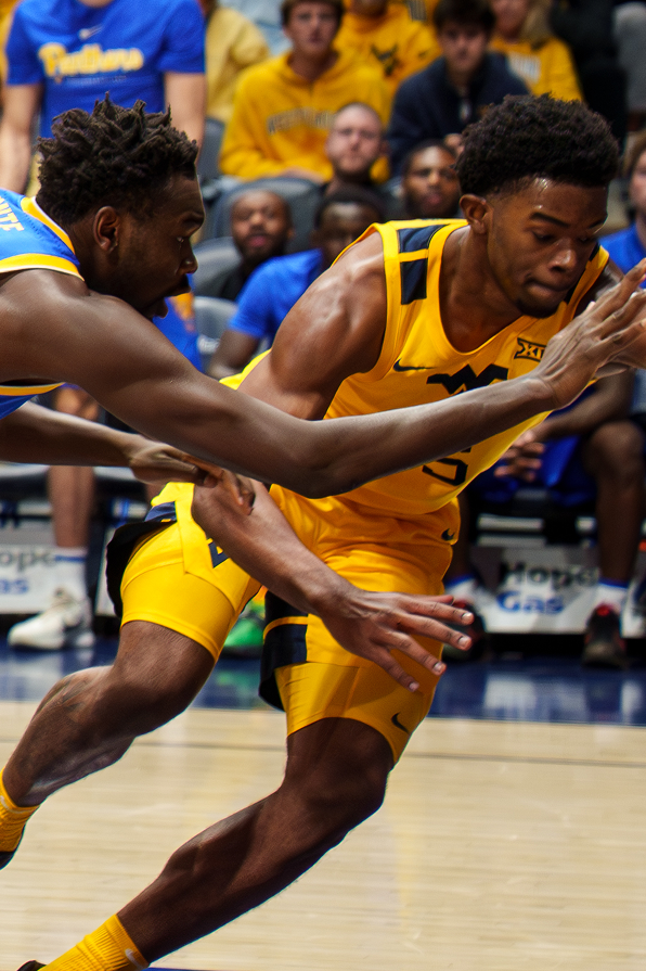  close up of West Virginia University basketball player being guarded by a pitt basketball player mid game
