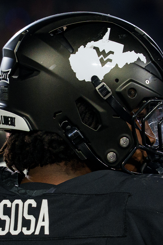 A close-up profile shot focusing on a West Virginia football player's matte black helmet and the back of his jersey, which reads SOSA in white lettering. The side of the helmet features a prominent white decal shaped like the state of West Virginia with a navy WV logo in the center, alongside dark chinstrap hardware and a Big 12 decal near the rear.