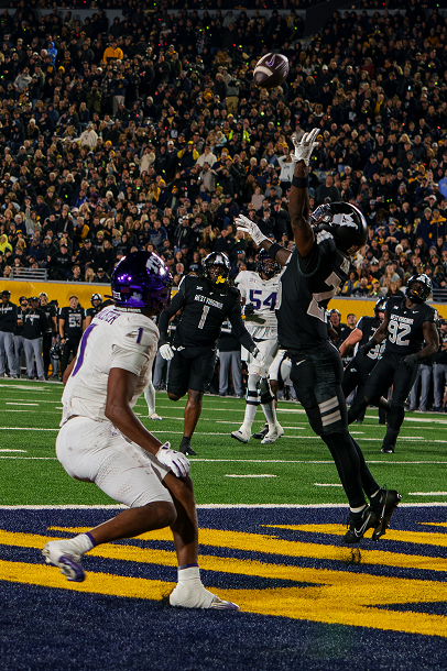 West Virginia University football player wearing a coal rush blackout jersey jumping up to almost catch a ball near the end zone while a tcu player gets near him